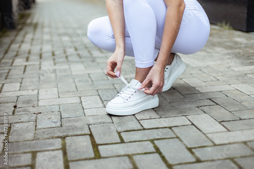 Fit woman in sports clothes ties the laces of sneakers in the city