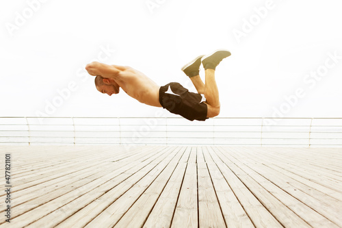 Muscular acrobatic man in flight over the floor on the beach