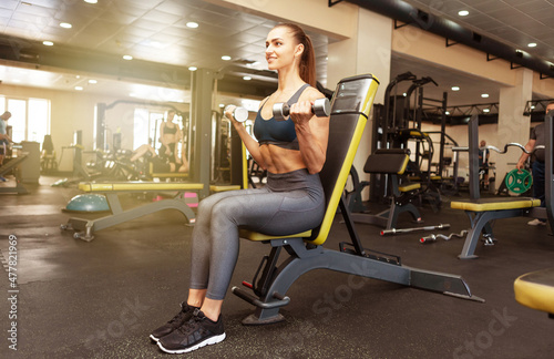 Athletic woman trains biceps with dumbbells in her hands in the gym. Healthy lifestyle
