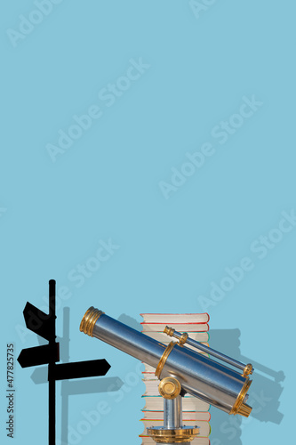 Cover page with an old antique metal telescope standing near a stack of books with a post showing directions at solid blue background with copy space and shadow. Concept exploration, education travel.