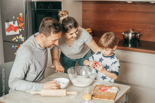 Attractive young woman Looking with pleasure her men knead dough for baking cookies. Dad and boy 4 years work together in team  mom teaches how to cook