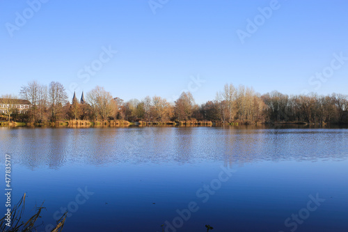 View over lake on bare trees against blue clear winter sky and church - Nettetal (Lobberich), Germany photo
