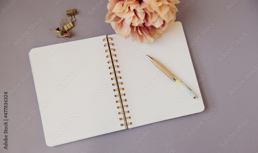 Cahier à spirale ouvert sur une page blanche avec un stylo, des pinces  dorées et une fleur rose sur fond mauve - inspiration pour l'écriture et  motivation pour le travail Stock Photo