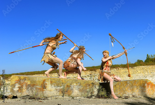 Three girls are dressed as Stoneage warriors. They 
are covered with mud and dirt and are seen attacking, 
screaming and shouting as they run over large boulders