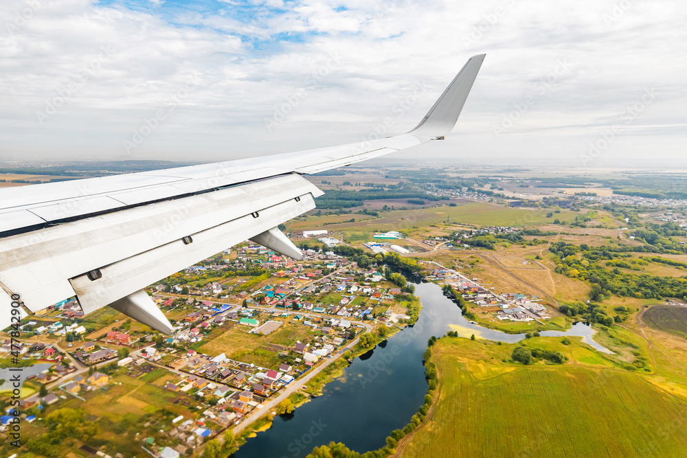 view from the passenger seat to the wing of the plane flying over lake and village in the countryside view from the passenger seat to the wing of the plane flying over lake and village in the countryside