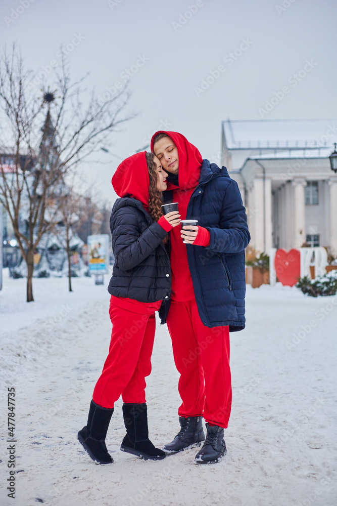young family guy and girl spend the day in the park on a snowy day. the guy hugs the girl while standing on the street, they drink coffee together.