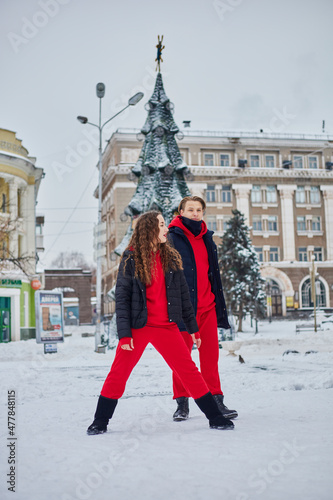 Fototapeta Naklejka Na Ścianę i Meble -  young family guy and girl spend the day in the park on a snowy day. Emotional young couple having fun while walking in the winter city, a lively man hugs his laughing beautiful woman.