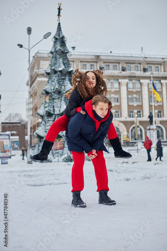 young family guy and girl spend the day in the park on a snowy day. Emotional young couple having fun while walking in the winter city, a lively man hugs his laughing beautiful woman.