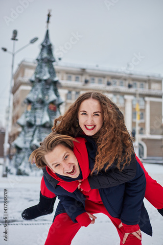 young family guy and girl spend the day in the park on a snowy day. Emotional young couple having fun while walking in the winter city, a lively man hugs his laughing beautiful woman.