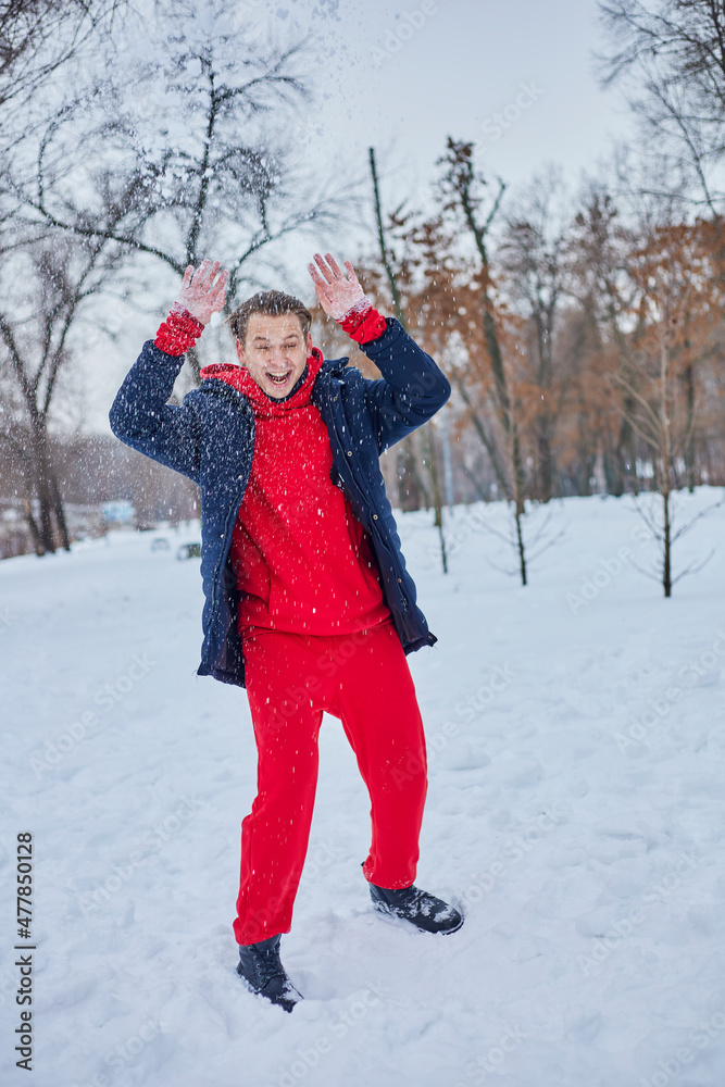 a young happy man is having fun in a winter park, throwing snow, it is cold in his hands, the emissions are off scale.