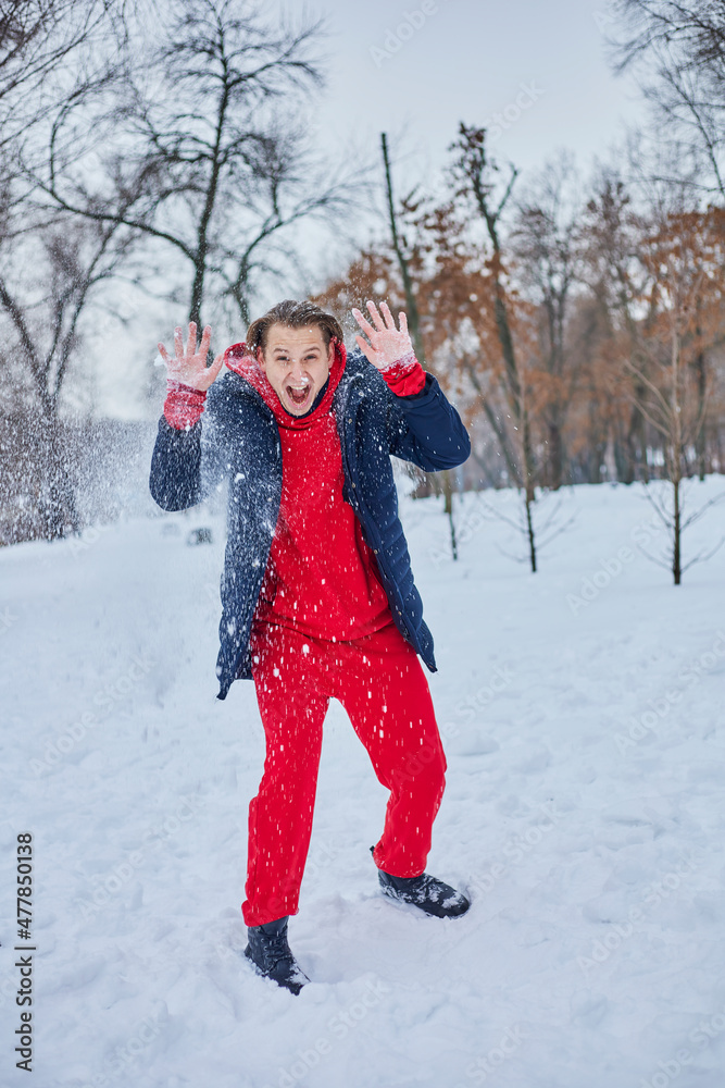 a young happy man is having fun in a winter park, throwing snow, it is cold in his hands, the emissions are off scale.