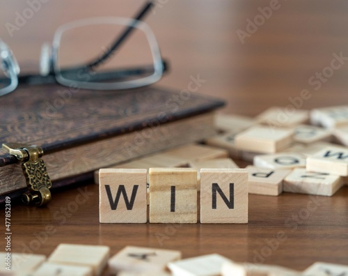 win concept represented by wooden letter tiles on a wooden table with glasses and a book