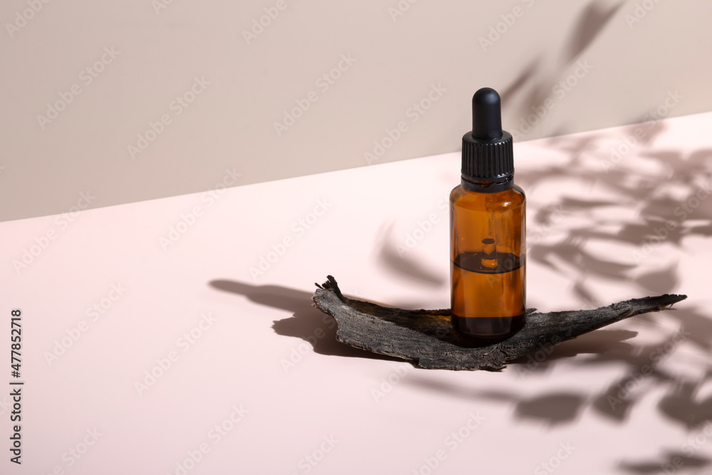 Dropper bottles essential oil with hard plant shadows and tree bark on pastel neutral pink background Dropper bottles essential oil with hard plant shadows and tree bark on pastel neutral pink background