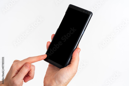Hands with phone close-up. Girl points her finger at smartphone screen. Women's hands with switched off mobile gadget. Black phone for application demonstration. Cellphone on light background