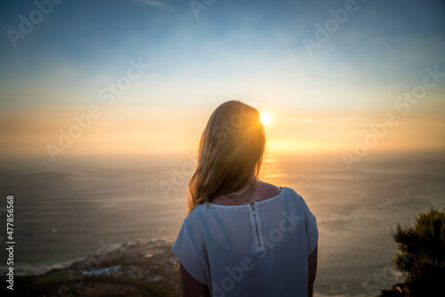 A young woman looking into sunset on a mountain