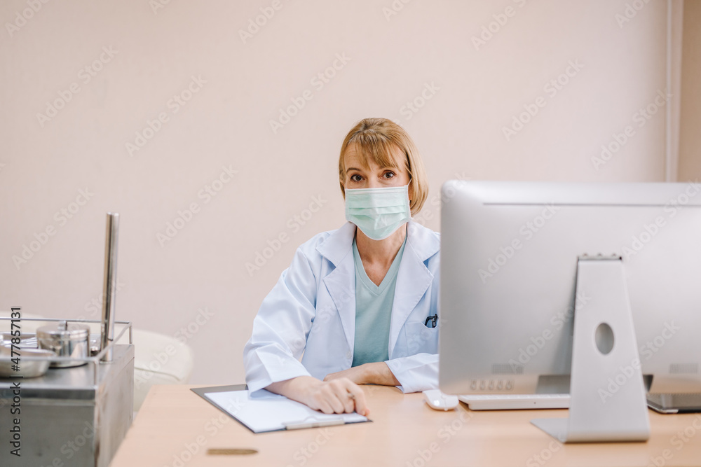 A female dentist sits in her office and looks at the camera in a friendly manner.
