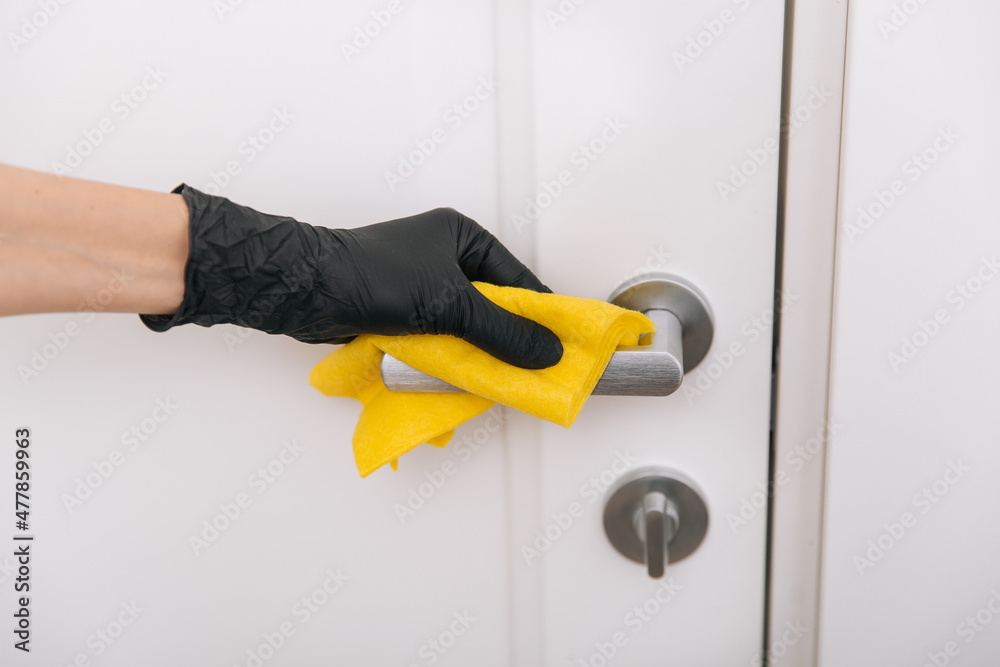 Cleaning door handle with yellow wipe in black gloves. Woman hand using towel for cleaning. Disinfection in hospital and public spaces against corona virus