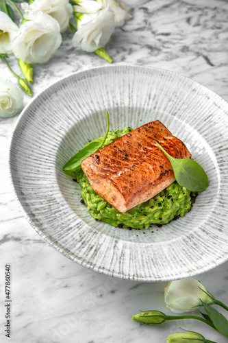 Grilled salmon fillet in avocado sauce in a festive plate on a marble background. Restaurant banquet menu.