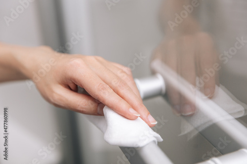 Cleaning glass door handles with an antiseptic wet wipe. Woman hand using towel for cleaning home room door link. Sanitize surfaces prevention in hospital and public spaces against corona virus © mlphoto