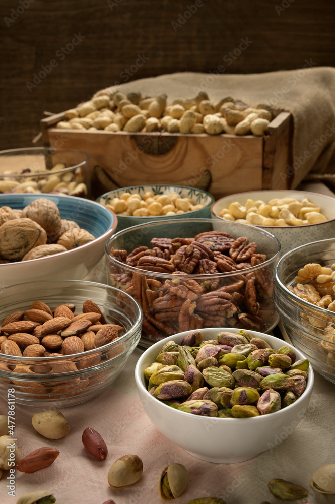 Different nuts and bowls closeup on a wooden table and brown background. Peanut, nut, cashew, almond, hazelnut, pistachio