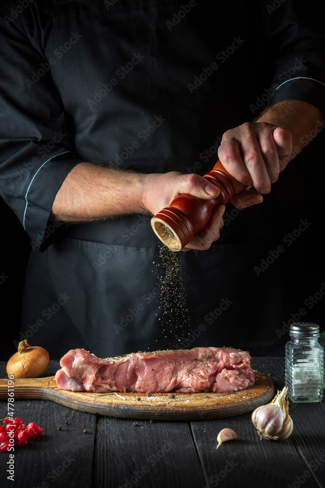 The chef prepares raw veal meat. Before baking, the chef adds pepper to the beef. National dish is being prepared in the restaurant kitchen.