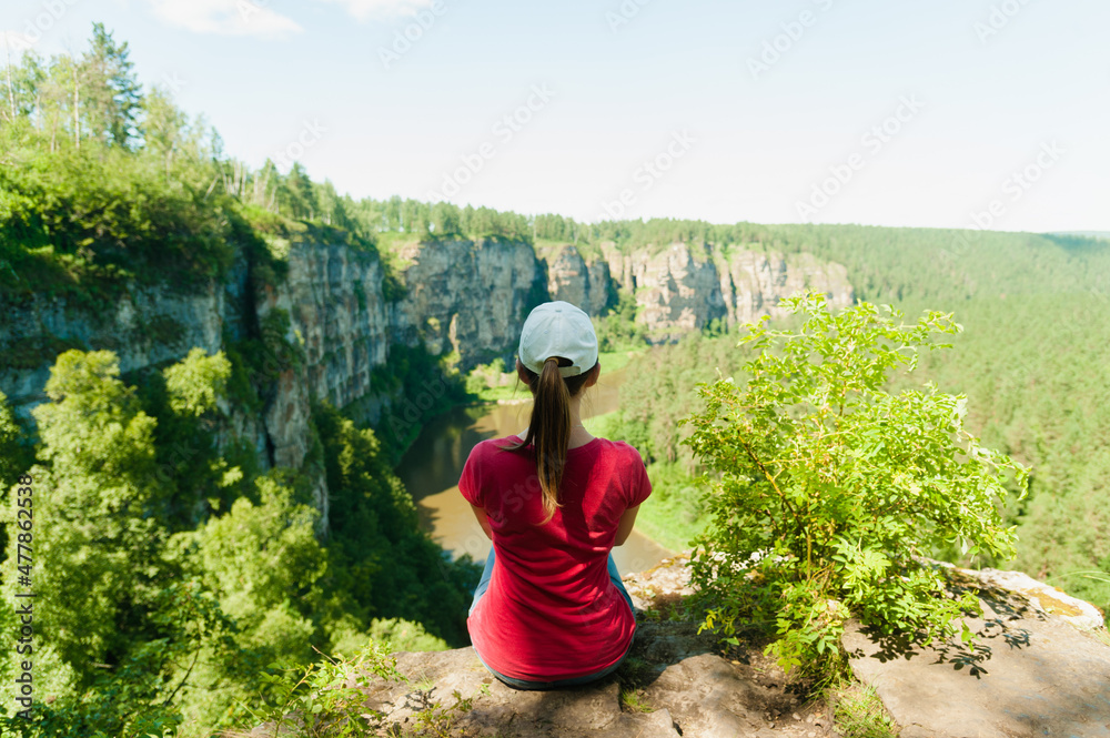 A young girl in a red T-shirt and a cap enjoys the beautiful view of the river in the canyon.
