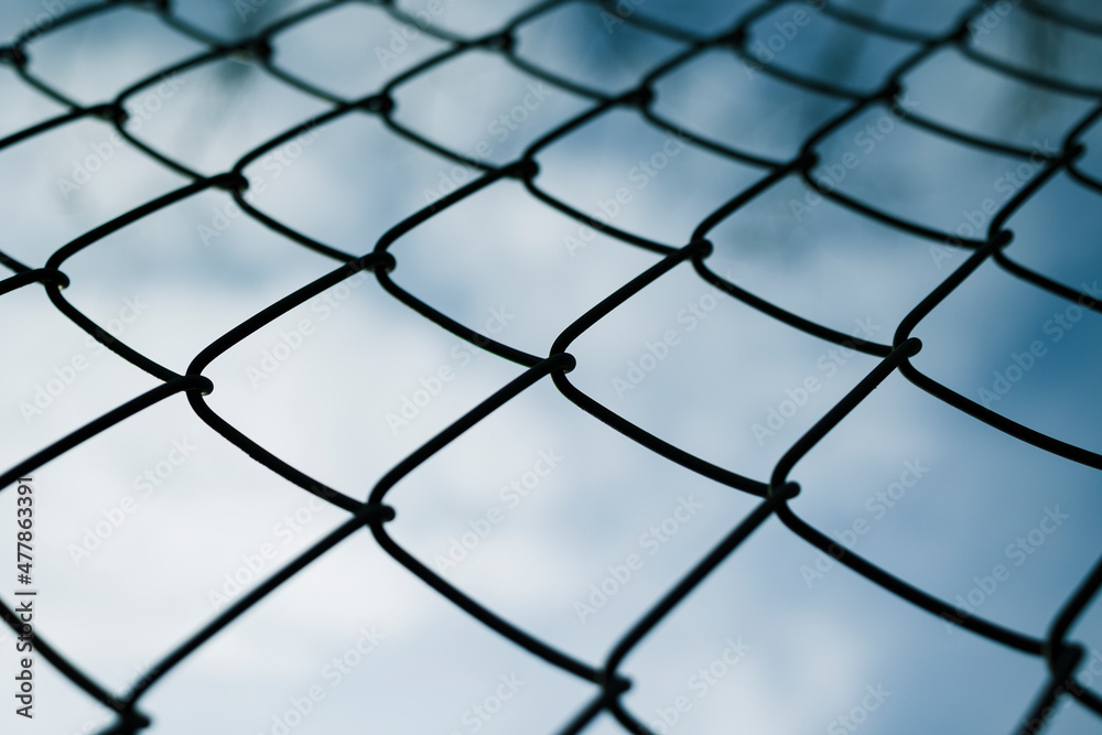 Dramaic blue sky with white clouds through a metal grid chain fence . low angle view Dramaic blue sky with white clouds through a metal grid chain fence . low angle view