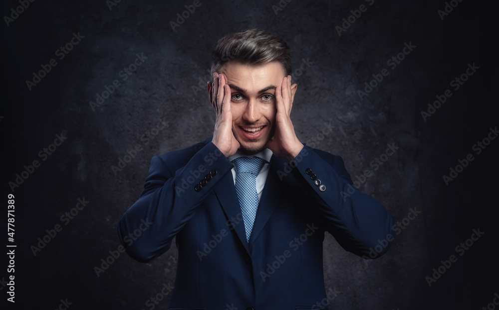 Young businessman man scared in a state of anxiety and daze holding his head with his hands on a dark background.