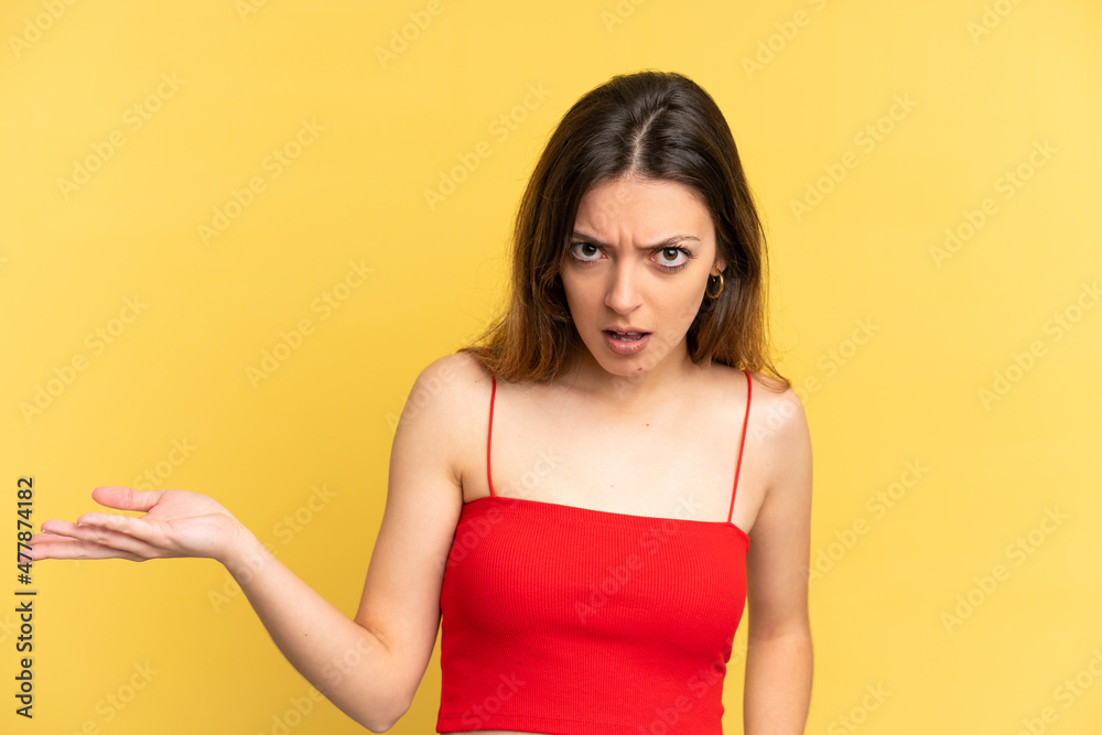 Young caucasian woman isolated on yellow background making doubts gesture Young caucasian woman isolated on yellow background making doubts gesture