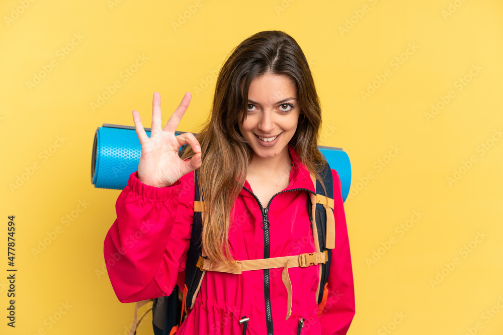 Young mountaineer man with a big backpack isolated on yellow background showing ok sign with fingers Young mountaineer man with a big backpack isolated on yellow background showing ok sign with fingers