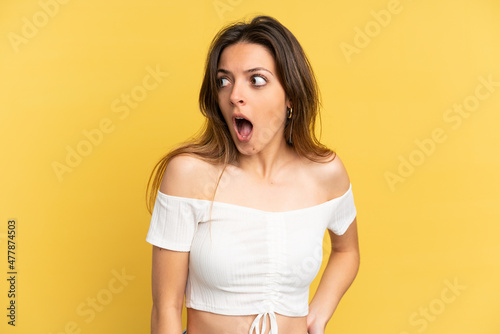 Young caucasian woman isolated on yellow background doing surprise gesture while looking to the side