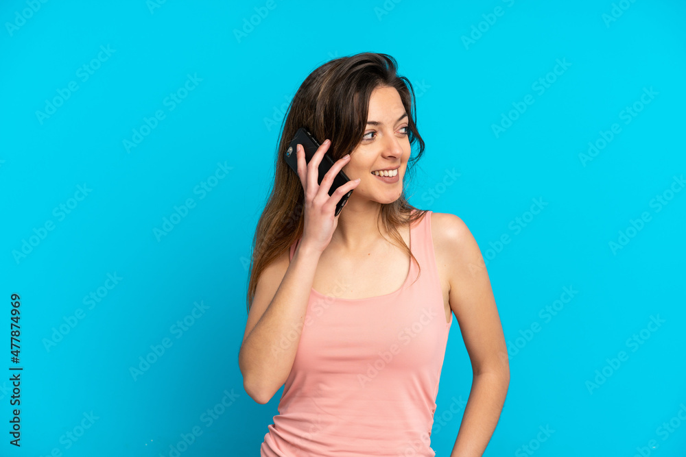 Young caucasian woman using mobile phone isolated on blue background looking side