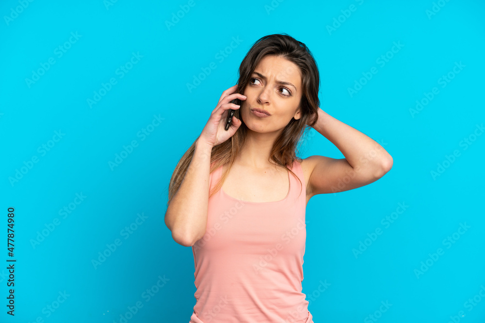 Young caucasian woman using mobile phone isolated on blue background having doubts