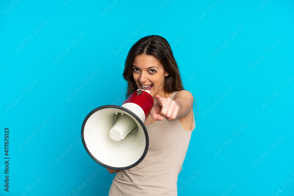 Young caucasian woman isolated on blue background shouting through a megaphone to announce something while pointing to the front Young caucasian woman isolated on blue background shouting through a megaphone to announce something while pointing to the front