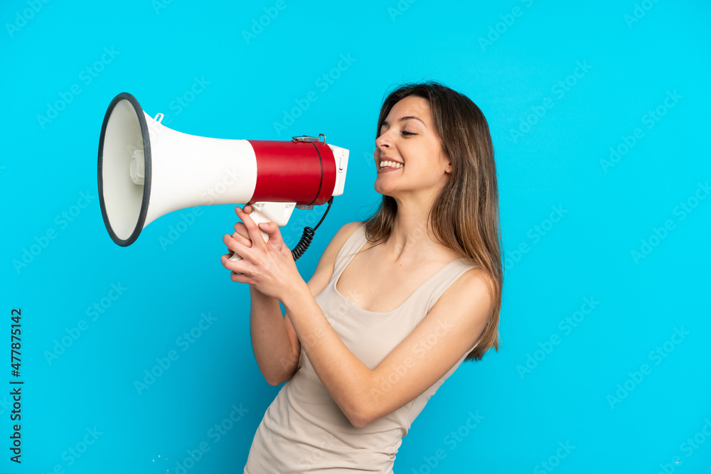 Young caucasian woman isolated on blue background shouting through a megaphone to announce something Young caucasian woman isolated on blue background shouting through a megaphone to announce something