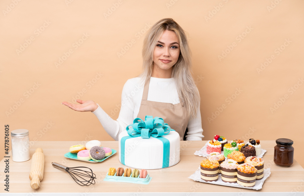 Teenager pastry chef with a big cake in a table holding copyspace imaginary on the palm Teenager pastry chef with a big cake in a table holding copyspace imaginary on the palm