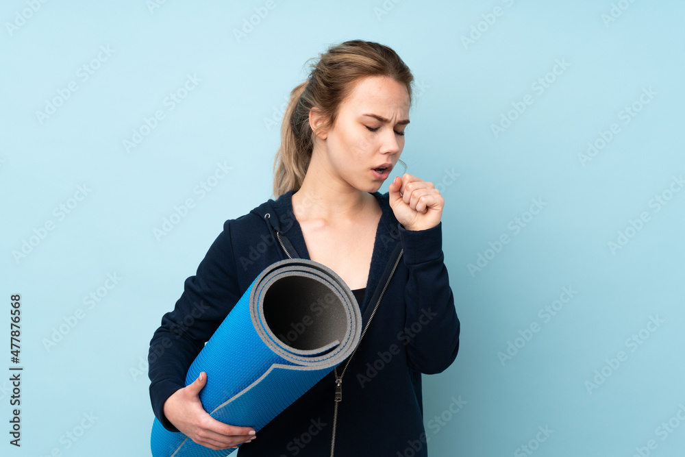 Teenager Russian girl holding mat isolated on blue background is suffering with cough and feeling bad Teenager Russian girl holding mat isolated on blue background is suffering with cough and feeling bad