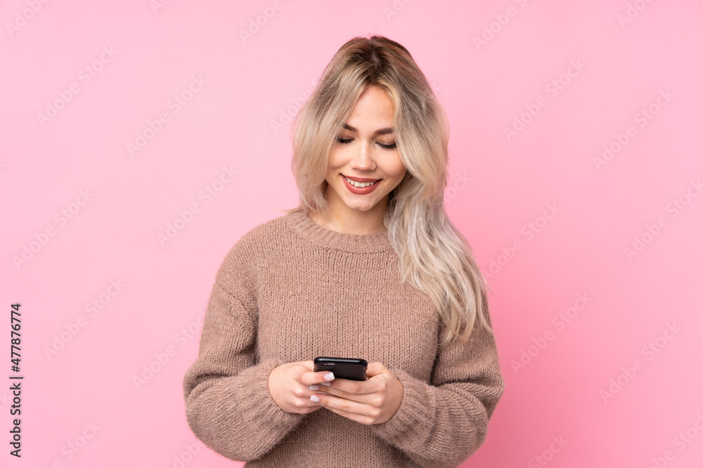 Teenager blonde girl wearing a sweater over isolated pink background sending a message with the mobile Teenager blonde girl wearing a sweater over isolated pink background sending a message with the mobile