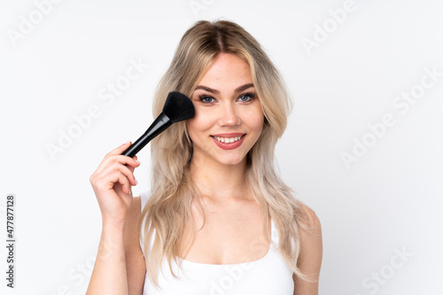 Teenager blonde girl over isolated white background holding makeup brush