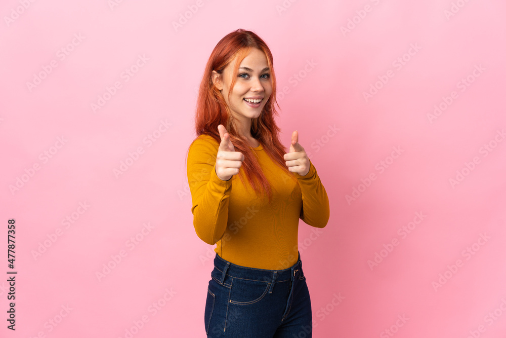 Teenager Russian girl isolated on pink background surprised and pointing front