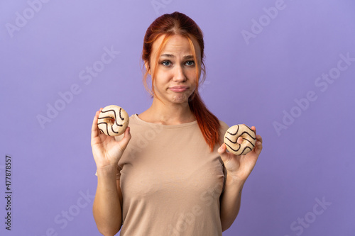 Teenager Russian girl isolated on purple background holding donuts with sad expression