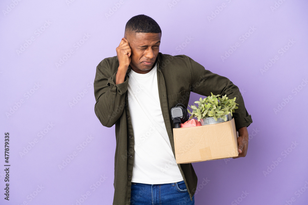Latin man making a move while picking up a box full of things frustrated and covering ears Latin man making a move while picking up a box full of things frustrated and covering ears