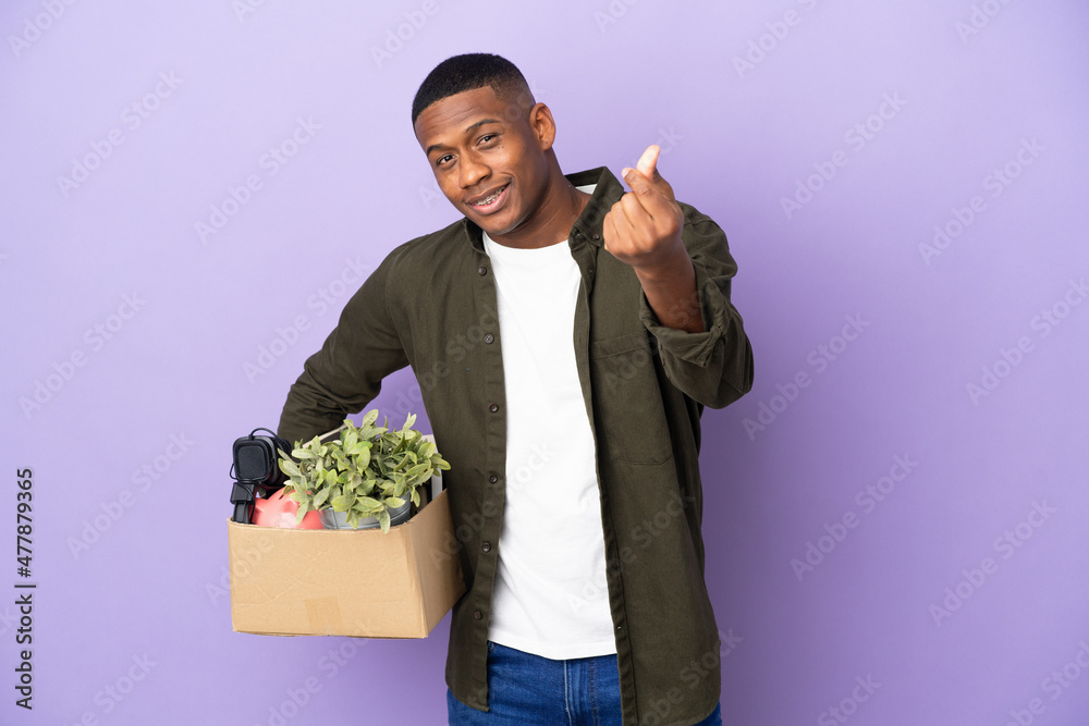 Latin man making a move while picking up a box full of things making money gesture Latin man making a move while picking up a box full of things making money gesture