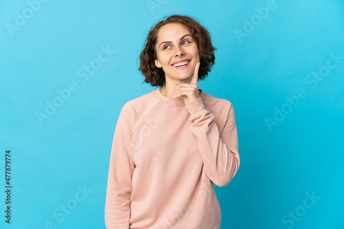 Young English woman isolated on blue background thinking an idea while looking up