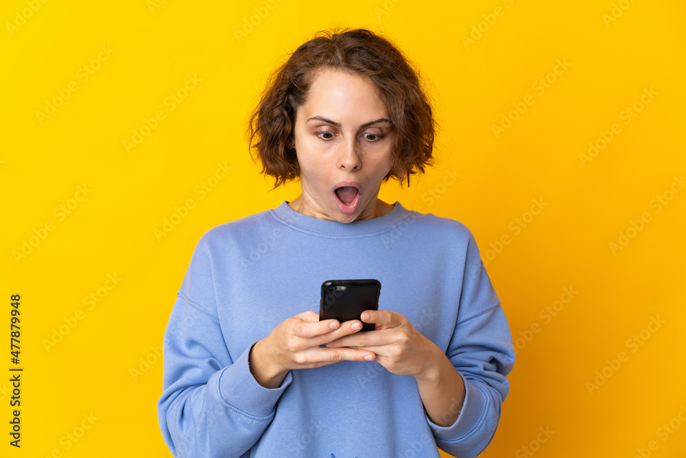 Young English woman isolated on pink background looking at the camera while using the mobile with surprised expression Young English woman isolated on pink background looking at the camera while using the mobile with surprised expression