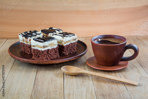 Pieces of delicious chocolate cake with cream and chocolate fondant in a plate and a cup of coffee on a wooden table