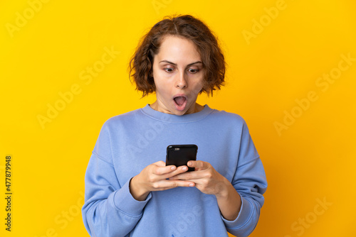 Young English woman isolated on pink background looking at the camera while using the mobile with surprised expression