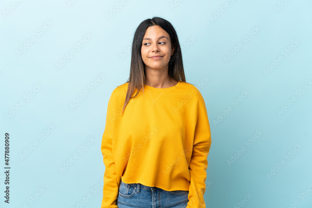 Caucasian girl isolated on blue background having doubts while looking side Caucasian girl isolated on blue background having doubts while looking side