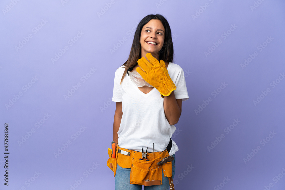 Young electrician woman isolated on purple background looking up while smiling Young electrician woman isolated on purple background looking up while smiling