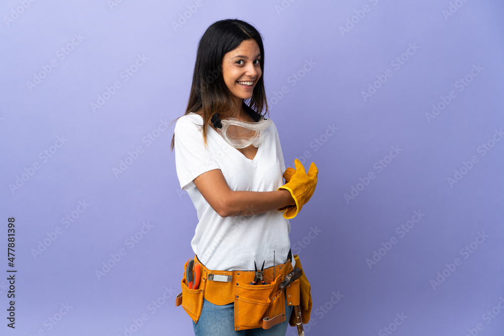 Young electrician woman isolated on purple background pointing back Young electrician woman isolated on purple background pointing back
